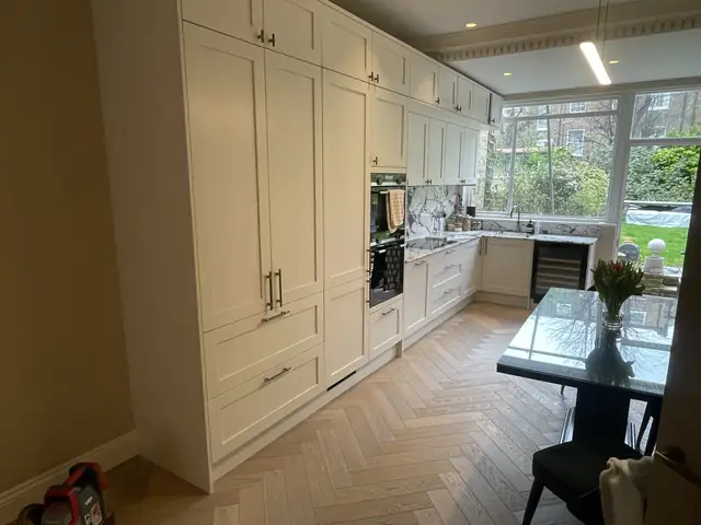 Spacious cream kitchen with tall cabinets, integrated appliances, and black dining table.